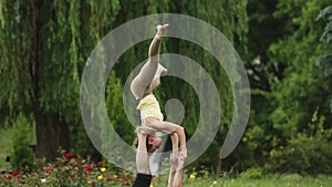 Beautiful couple practicing acro yoga. Young yoga instructors practice in a city park on green grass. Two successful