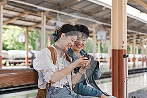 Beautiful couple at railway station waiting for the train. A young woman and a man are sitting and looking at pictures