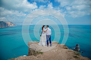 Beautiful couple on the sea rocks in wedding dress. Just married view from behind