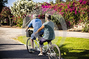 Beautiful couple of senior and mature married, riding a doble bike, tandem, together to have fun with a great and sunny day -