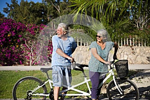 Beautiful couple of senior and mature married, riding a doble bike, tandem, together to have fun with a great and sunny day -