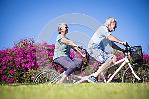 Beautiful couple of senior and mature married, riding a doble bike, tandem, together to have fun with a great and sunny day -