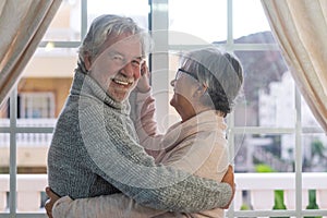 A beautiful couple of senior people hugging while dancing in front of the window. Two active retirees are having fun