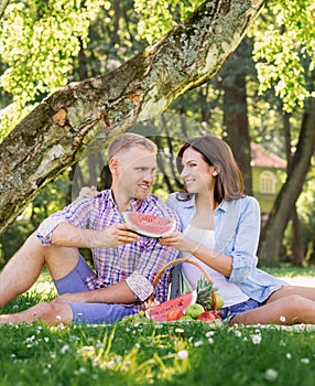 Beautiful couple sharing a slice of watermelon in the park while having a picnic.