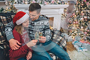 Beautiful couple sits together and holds glasses of champaigne. Young man embrace woman. She looks at glasses. They sit