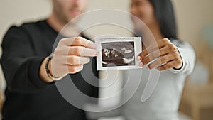 Beautiful couple sitting on bed holding baby ultrasound smiling at bedroom