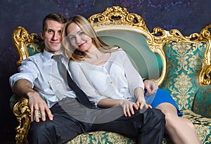 Beautiful couple sitting on classic sofa. Girl and boy on green sofa. Happy married couple. Successful people in vintage interior