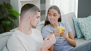 Beautiful couple sitting on sofa together drinking coffee at home