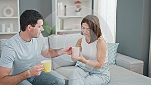 Beautiful couple sitting on sofa together drinking coffee smiling at home