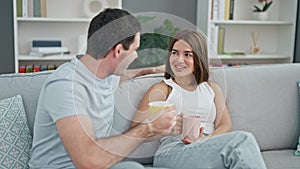 Beautiful couple sitting on sofa together drinking coffee smiling at home