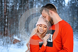 Beautiful couple standing arm in arm in the red sweater in the background of the forest in winter , a walk in the winter woods