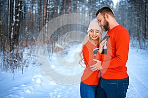 Beautiful couple standing arm in arm in the red sweater in the background of the forest in winter , a walk in the winter woods