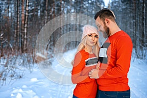 Beautiful couple standing arm in arm in the red sweater in the background of the forest in winter , a walk in the winter woods