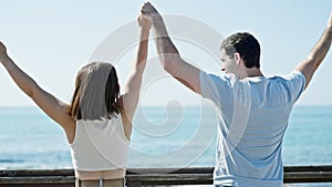 Beautiful couple standing backwards with hands raised up at seaside