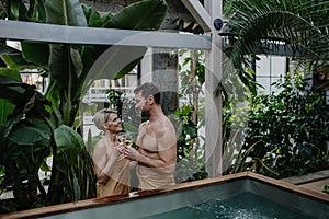 Beautiful couple standing hot tub, toasting, drinking champagne, enjoying romantic wellness weekend in spa. Concept
