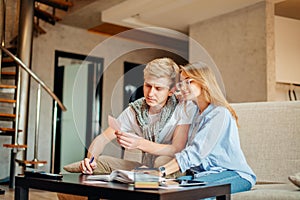 Couple students studying, reading book while sitting on sofa