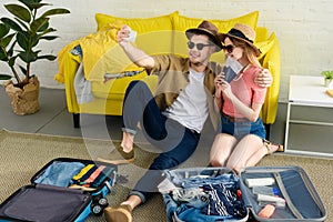 beautiful couple taking selfie on smartphone while packing suitcases