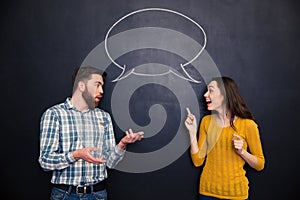 Beautiful couple talking over blackboard background with speech bubble