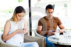 Beautiful couple using their mobile phones while sitting at cafe