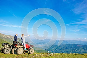 Beautiful couple is watching the sunset from the mountain sitting on atv quadbike