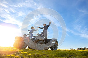 Beautiful couple is watching the sunset from the mountain sitting on atv quadbike