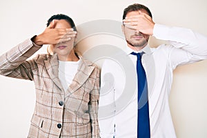 Beautiful couple wearing business clothes covering eyes with hand, looking serious and sad