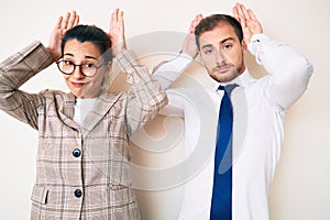 Beautiful couple wearing business clothes doing bunny ears gesture with hands palms looking cynical and skeptical