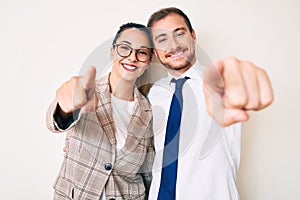 Beautiful couple wearing business clothes pointing to you and the camera with fingers, smiling positive and cheerful