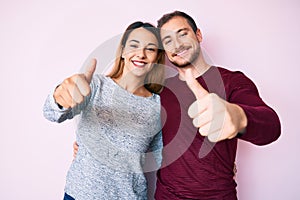 Beautiful couple wearing casual clothes approving doing positive gesture with hand, thumbs up smiling and happy for success