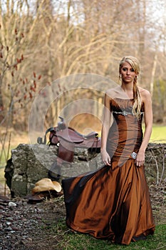 Beautiful cowgirl in a formal dress near a cement wall