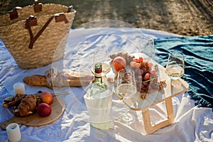 Beautiful cozy autumn picnic by the lake with fruits, pastries and wine. Sun rays. Sunset