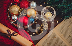 Beautiful cozy christmas scene with xmas tree branch, a small basket with colorful balls, a burning candle, opened book, rolled