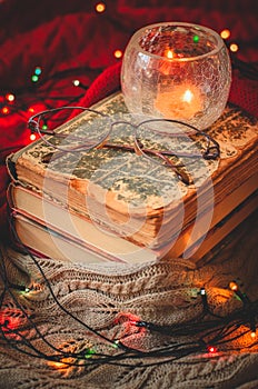 Beautiful cozy christmas winter scene with a stack of books, eyeglasses, a burning candle and glowing xmas garland