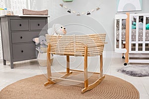 Beautiful cradle with toy rabbit near crib and dresser in baby room. Interior design