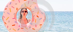 Beautiful crazy woman is posing with a doughnut inflatable ring asnd showing her tongue at the sea background