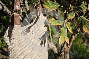 Beautiful cream crocheted handbag with brown handle and nature leaves behind the bush in the garden in summer