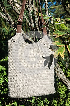 Beautiful cream crocheted handbag with brown handle and nature leaves behind the bush in the garden in summer