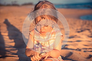 Beautiful curious child girl toddler playing on beach with hermit crab during summer vacation concept childhood lifestyle