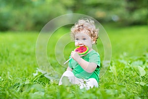 Beautiful curly baby girl eating watermelon candy