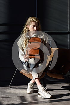 beautiful curly blond hair woman posing with a leather backpack