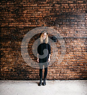 Beautiful curly girl in a bonnet standing against a brick wall