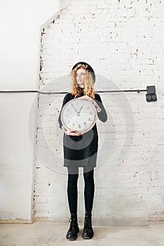 Beautiful curly girl holds a big clock in her hands