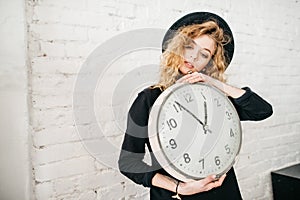 Beautiful curly girl holds a big clock in her hands