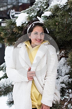 A beautiful curly-haired brunette in a white coat on the background of a Christmas tree in the snow.