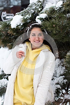 A beautiful curly-haired brunette in a white coat on the background of a Christmas tree in the snow.