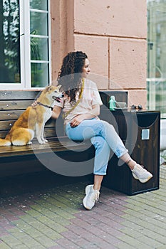 Beautiful curly-haired girl sitting in street cafe with cute dog smiling