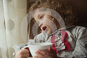 Beautiful curly-haired little girl with a cup