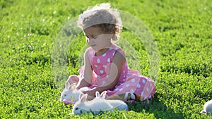 A beautiful curly little girl is playing with a white hare in the garden. The pet is a white bunny