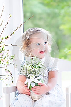 Beautiful curly toddler girl holding first spring flowers