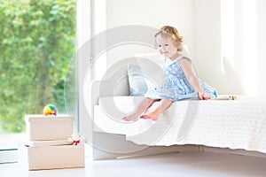 Beautiful curly toddler girl sitting on a white bed